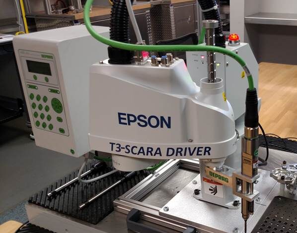 Schneider & Company - A Deprag Epson T3-SCARA driver industrial robot performing a task or demonstration on a workbench.