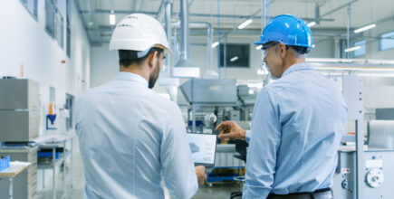 Schneider & Company - Two professionals wearing hard hats and discussing paperwork in an industrial setting.