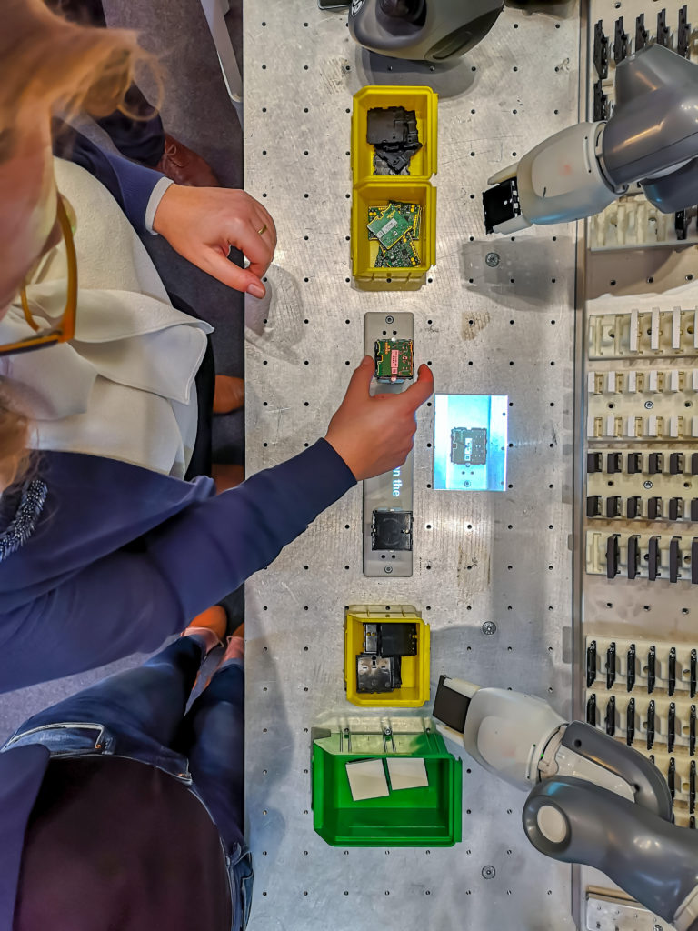 Caucasian female technician works alongside a collaborative robotic arm as they pick and place computer chips. 